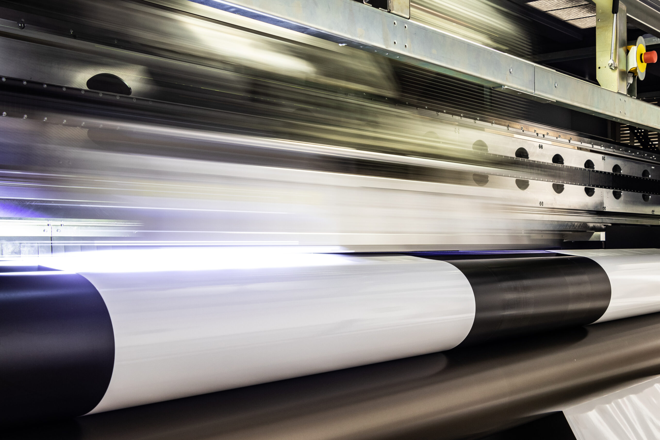 Massive print head flashing by while processing a big oversized roll of glossy premium paper in a professional plot and print facility.